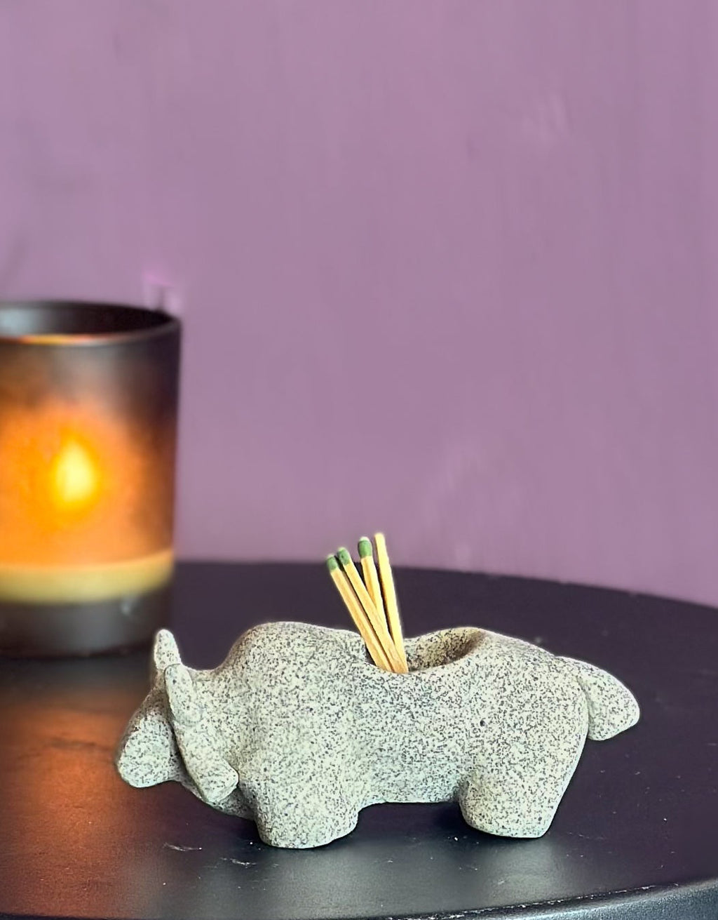 Decorative elephant match holder on a black table with a purple wall background